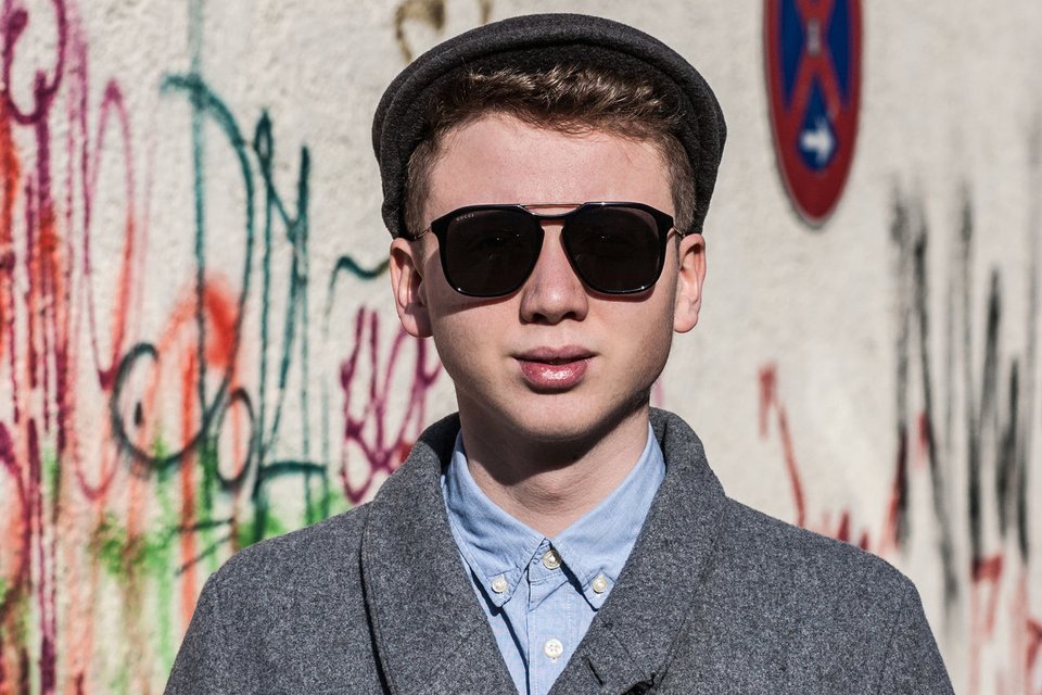 Junger Mann in grauem Mantel, Schiebermütze und dunkler Sonnenbrille
