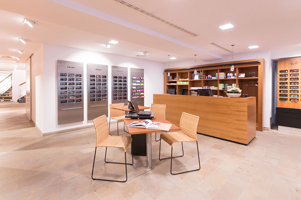 Helles Optikgeschäft mit Beratungstisch, Empfang und Brillenwänden Prada, Armani, Gucci, Ray-Ban