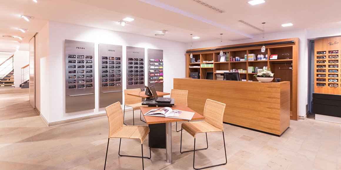 Helles Optikgeschäft mit Beratungstisch, Empfang und Brillenwänden Prada, Armani, Gucci, Ray-Ban