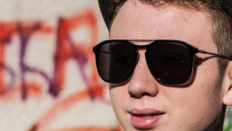 Junger Mann mit dunkler Sonnenbrille grauem Hut und grauem Mantel