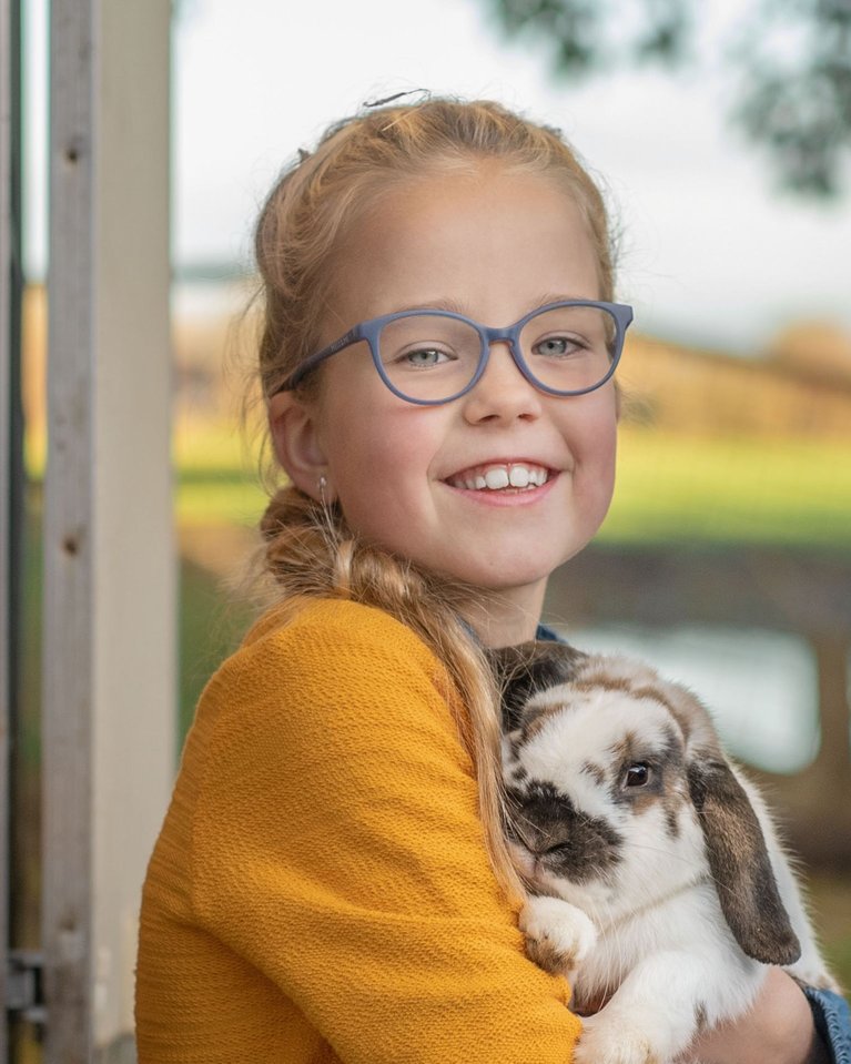 Smiling young girl wearing blue glasses hugging spotted rabbit