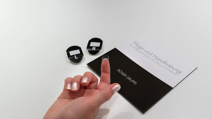 Kontaktlinse auf dem Finger neben Broschüre Pflege und Handhabung DÖSER GRUPPE