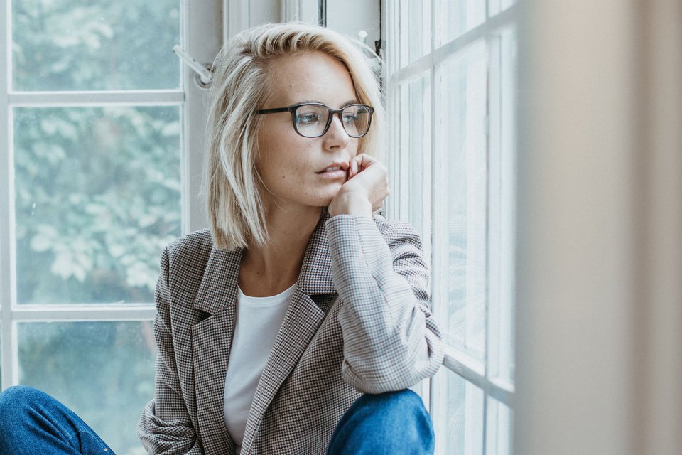 Frau mit Brille sitzt am Fenster neben HOFFMANN NATURAL EYEWEAR